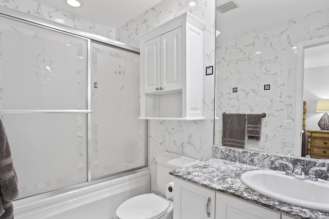 full bathroom featuring vanity, tile walls, enclosed tub / shower combo, and toilet