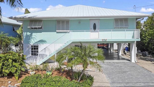 coastal inspired home featuring metal roof, stairs, decorative driveway, a porch, and a carport