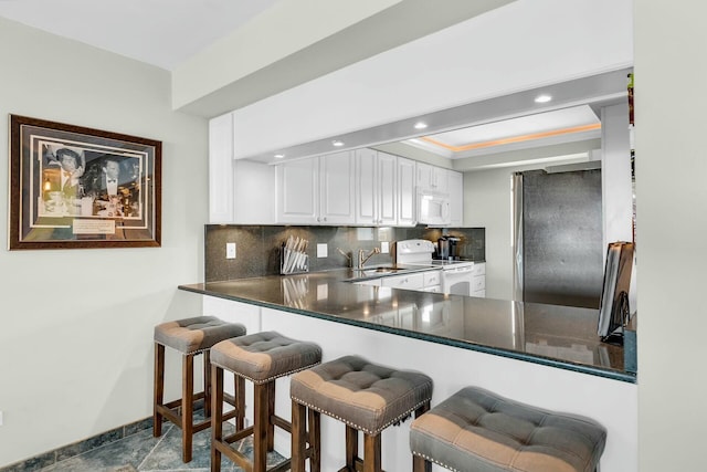 kitchen featuring white appliances, white cabinetry, tasteful backsplash, a tray ceiling, and kitchen peninsula