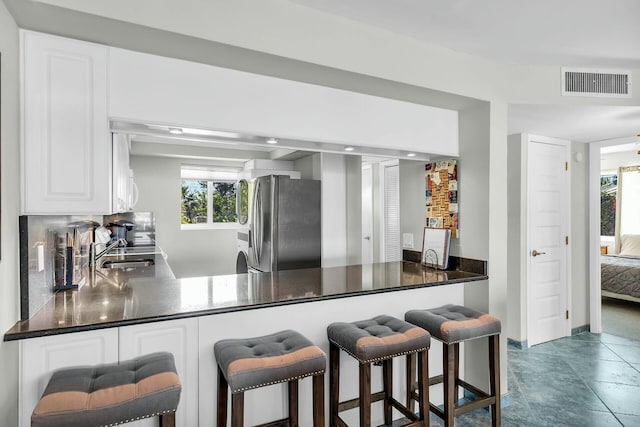 kitchen featuring stainless steel refrigerator, white cabinetry, sink, decorative backsplash, and kitchen peninsula