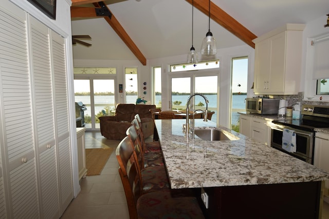 kitchen with stainless steel appliances, a water view, a kitchen island with sink, and white cabinets