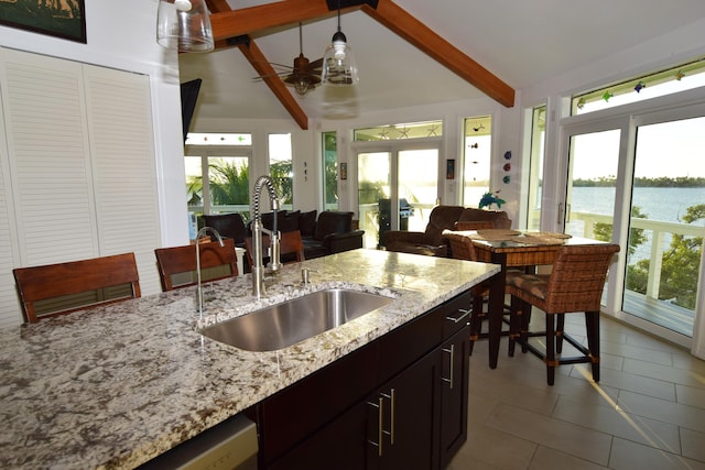 kitchen featuring sink, hanging light fixtures, a water view, light stone counters, and lofted ceiling with beams