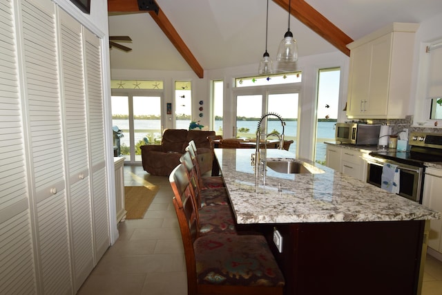 kitchen featuring appliances with stainless steel finishes, sink, hanging light fixtures, a kitchen island with sink, and a water view