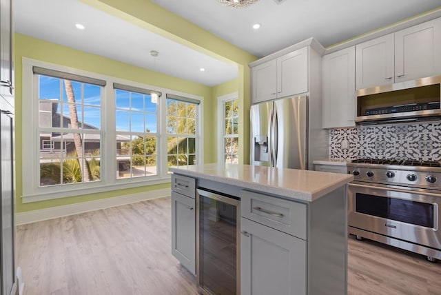 kitchen featuring light hardwood / wood-style flooring, hanging light fixtures, stainless steel appliances, tasteful backsplash, and beverage cooler