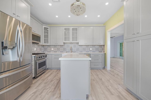 kitchen with a kitchen island, appliances with stainless steel finishes, tasteful backsplash, white cabinetry, and light hardwood / wood-style flooring