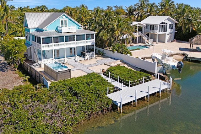 rear view of property featuring a hot tub, a patio, a water view, and a sunroom