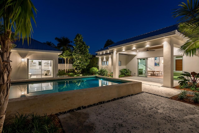 pool at night with a ceiling fan, an outdoor pool, and a patio