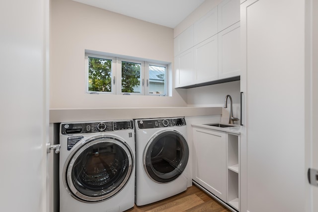 clothes washing area with wood finished floors, separate washer and dryer, a sink, and cabinet space