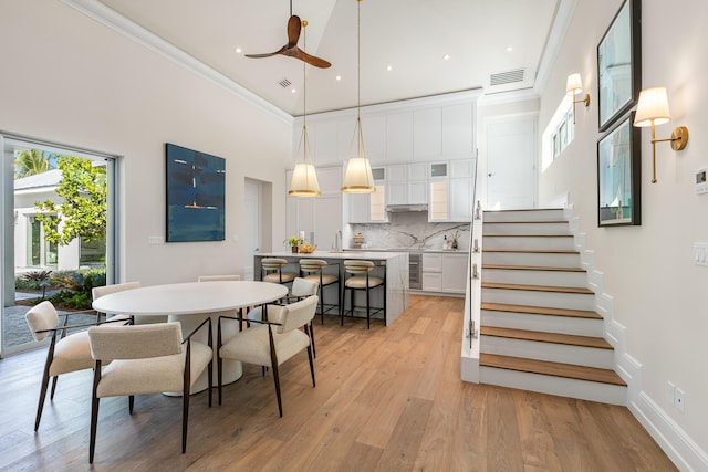 dining area featuring crown molding, visible vents, a towering ceiling, light wood-type flooring, and stairs