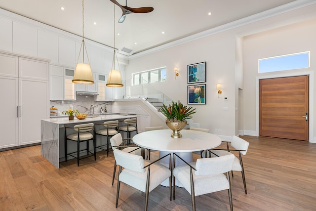 dining space featuring light wood finished floors, ceiling fan, and crown molding