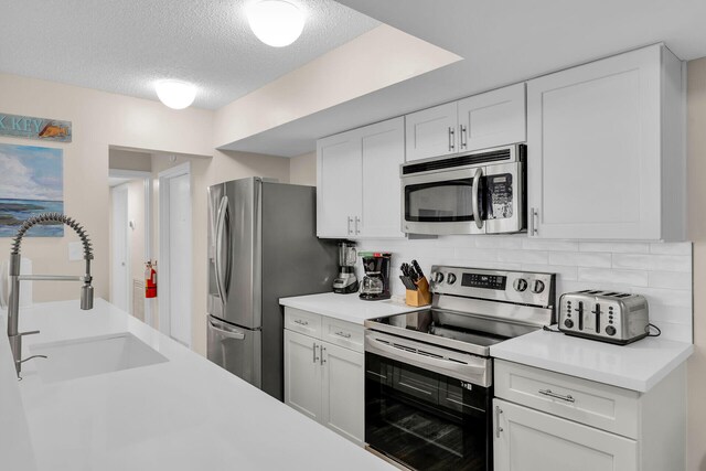 kitchen with sink, white cabinetry, stainless steel appliances, a textured ceiling, and decorative backsplash