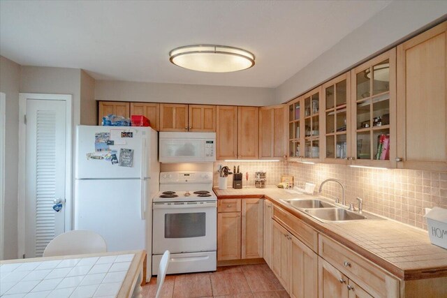 kitchen featuring tile counters, backsplash, white appliances, and a sink