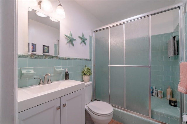 full bath with a wainscoted wall, toilet, tile walls, a shower stall, and vanity