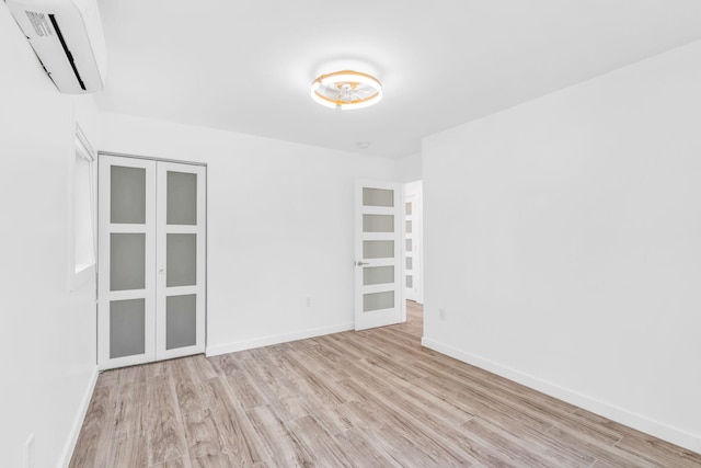 unfurnished room with a wall mounted AC, baseboards, and wood finished floors