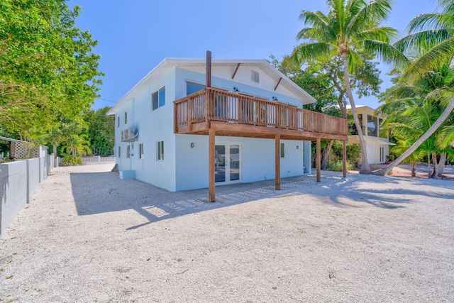 rear view of property featuring french doors, fence, a wooden deck, and stucco siding