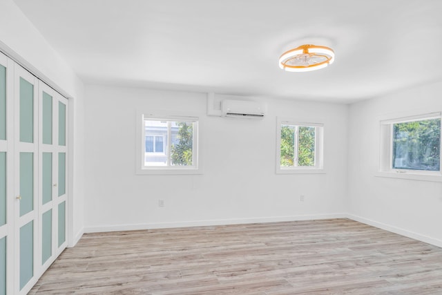 spare room featuring a healthy amount of sunlight, baseboards, light wood-type flooring, and a wall unit AC