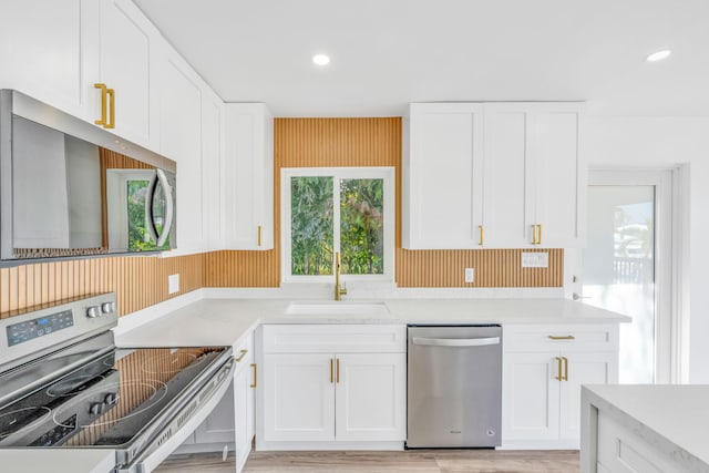 kitchen featuring recessed lighting, light wood-style floors, white cabinets, stainless steel appliances, and a sink