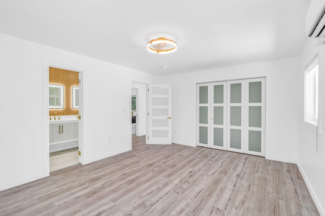 spare room featuring a wall mounted air conditioner, light wood-type flooring, and baseboards