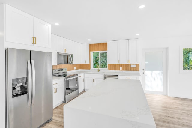 kitchen featuring light wood finished floors, white cabinets, stainless steel appliances, and light stone counters