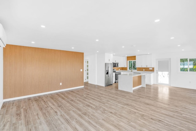 unfurnished living room featuring recessed lighting, light wood-style floors, baseboards, and wood walls