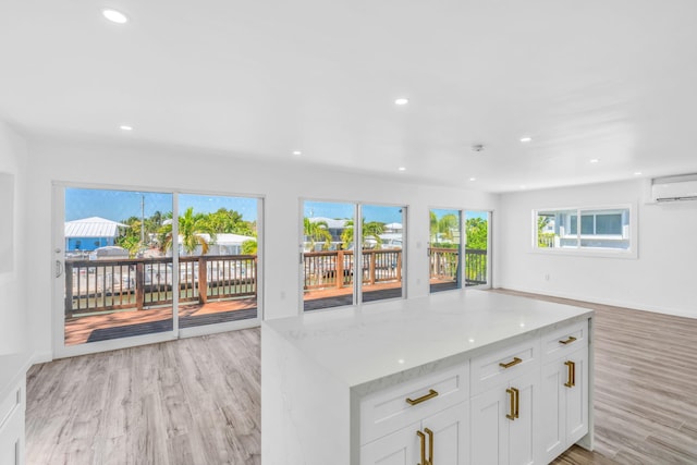 kitchen featuring an AC wall unit, light stone counters, open floor plan, and light wood-type flooring