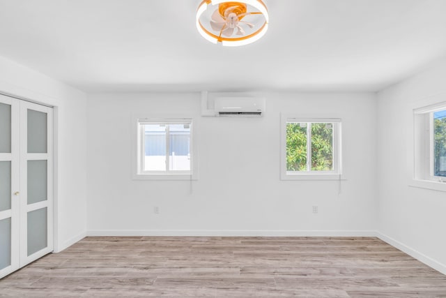 empty room with a wealth of natural light, baseboards, light wood-style flooring, and a wall mounted AC