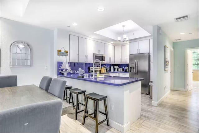 kitchen featuring a breakfast bar area, appliances with stainless steel finishes, backsplash, kitchen peninsula, and light wood-type flooring