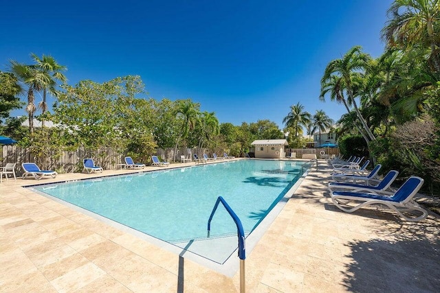 pool featuring a patio area, fence, an outdoor structure, and a storage shed