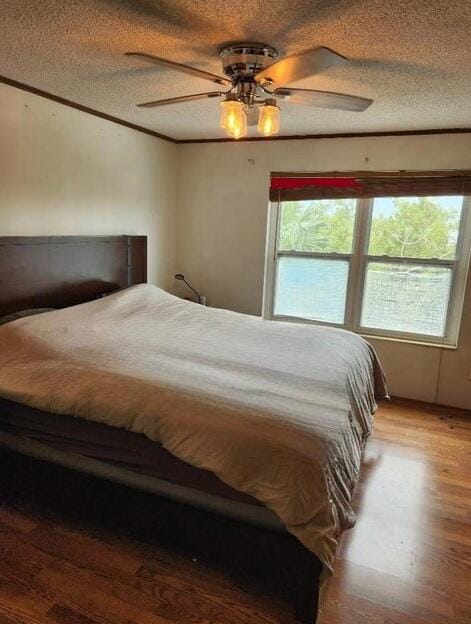 bedroom featuring ornamental molding, a ceiling fan, a textured ceiling, and wood finished floors