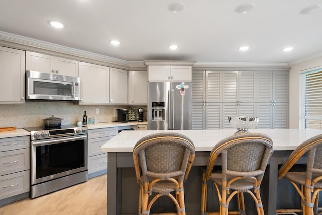 kitchen featuring stainless steel appliances, crown molding, gray cabinets, and a breakfast bar area