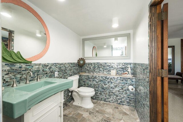 bathroom with vanity, toilet, tile walls, and a washtub