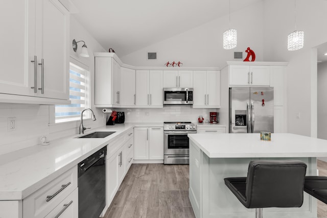 kitchen with sink, a breakfast bar area, appliances with stainless steel finishes, white cabinets, and decorative light fixtures