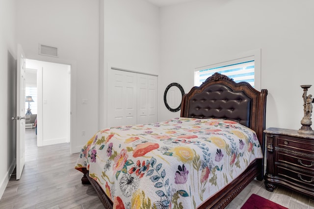 bedroom with a towering ceiling, light hardwood / wood-style floors, and a closet