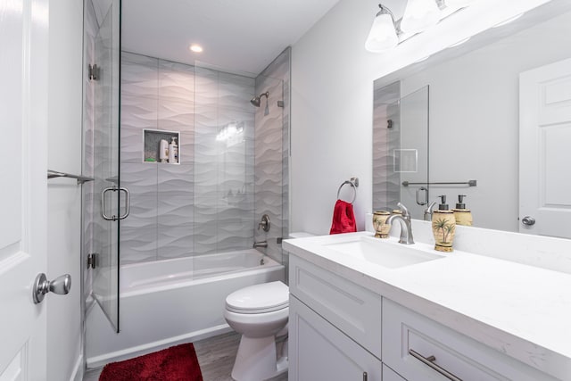 full bathroom featuring hardwood / wood-style flooring, bath / shower combo with glass door, vanity, and toilet