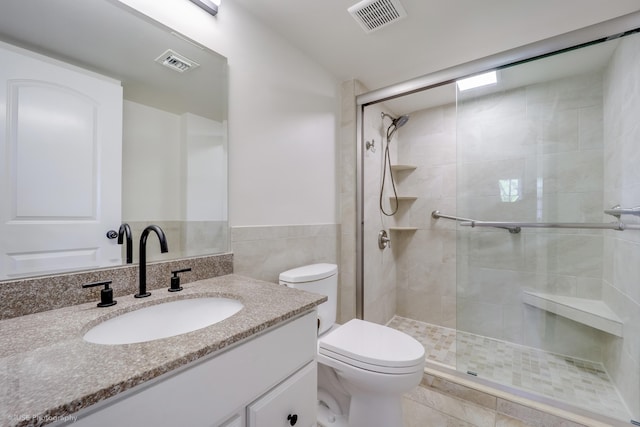 bathroom featuring vanity, toilet, a shower with door, and tile walls