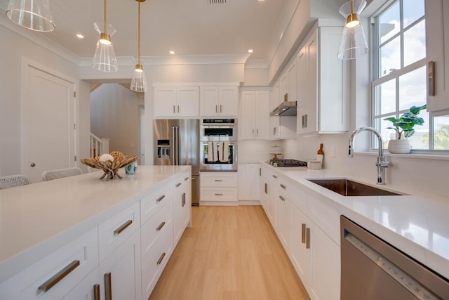 kitchen with appliances with stainless steel finishes, pendant lighting, sink, white cabinets, and light hardwood / wood-style flooring