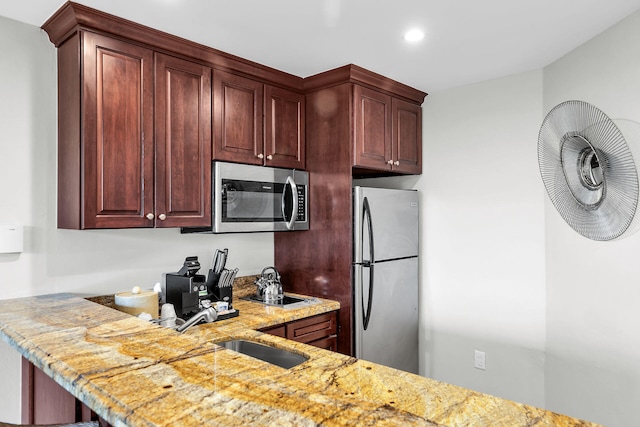 kitchen with reddish brown cabinets, light stone counters, stainless steel appliances, a sink, and recessed lighting