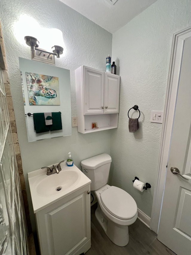 half bath with a textured wall, toilet, vanity, wood finished floors, and baseboards