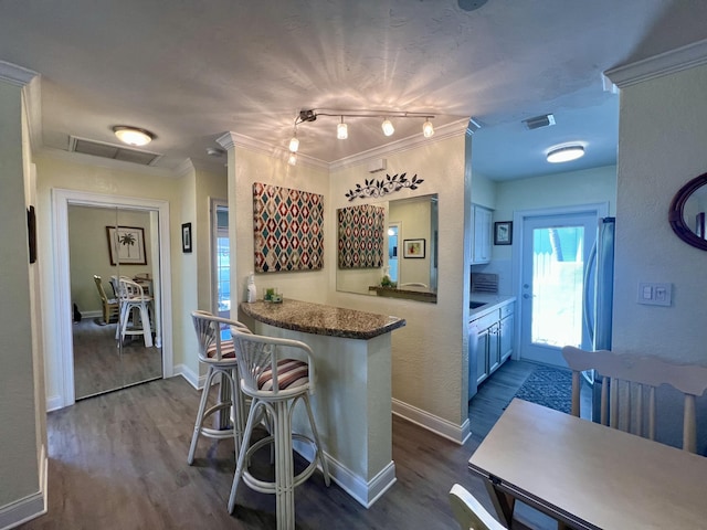 kitchen featuring dark wood-type flooring, crown molding, a peninsula, and a kitchen breakfast bar