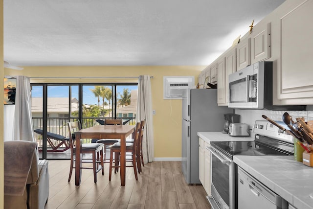 119 Cortez Dr Unit 8G, Islamorada, FL 33036 - kitchen with stainless steel appliances, tile counters, light wood-style flooring, baseboards, and a wall mounted air conditioner