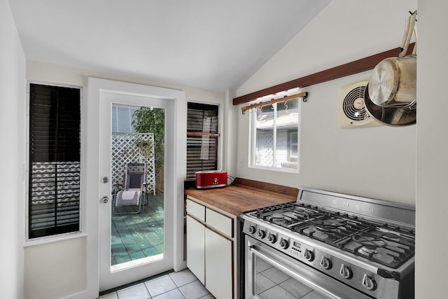 kitchen featuring stainless steel gas range oven, white cabinetry, lofted ceiling, wooden counters, and light tile patterned floors