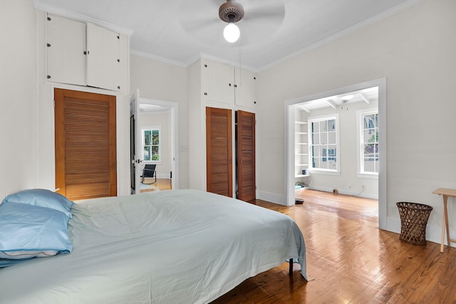 bedroom with crown molding, wood finished floors, multiple closets, ceiling fan, and baseboards