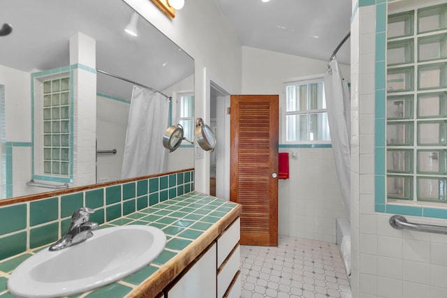 bathroom featuring tile walls, vaulted ceiling, vanity, and shower / tub combo with curtain