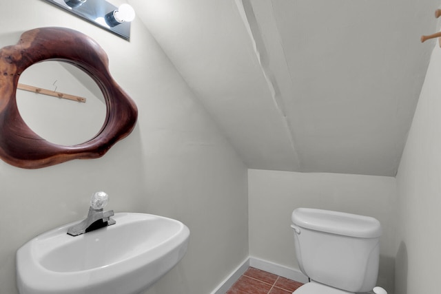 half bathroom with a sink, baseboards, toilet, lofted ceiling, and tile patterned flooring