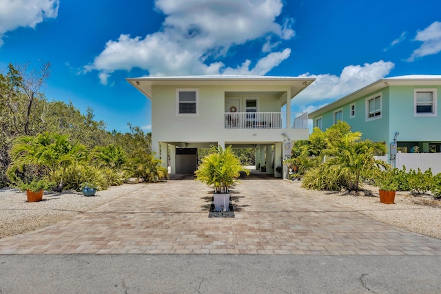 raised beach house with decorative driveway, a balcony, and a carport