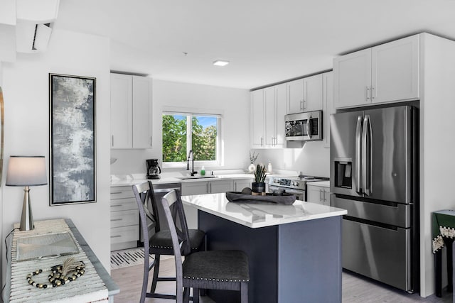 kitchen with sink, a center island, stainless steel appliances, light hardwood / wood-style floors, and white cabinets