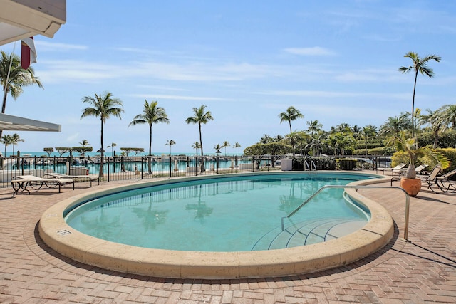 community pool with a water view, a patio, and fence