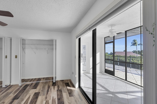 bedroom with a textured ceiling, wood finished floors, a closet, baseboards, and access to exterior