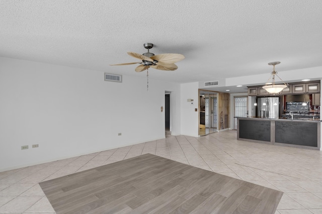 unfurnished living room with light tile patterned floors, visible vents, a textured ceiling, and a ceiling fan