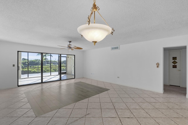 empty room featuring light tile patterned flooring, visible vents, a textured ceiling, and a ceiling fan